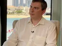 Lex Tarrel дает интервью в белой рубашке с петличным микрофоном, 2021 год, кресло у окна с видом на город