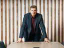Lex Tarrel стоит, опершись руками на переговорный стол, 2022 год, кабинет с деревянными рейками
